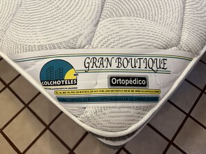 A hotel room with a bed covered in a white blanket with a label that reads "GRAN BOUTIQUE" and "COLCHOTEALES."