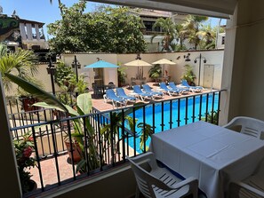 A balcony with a pool, lounge chairs, and a table.