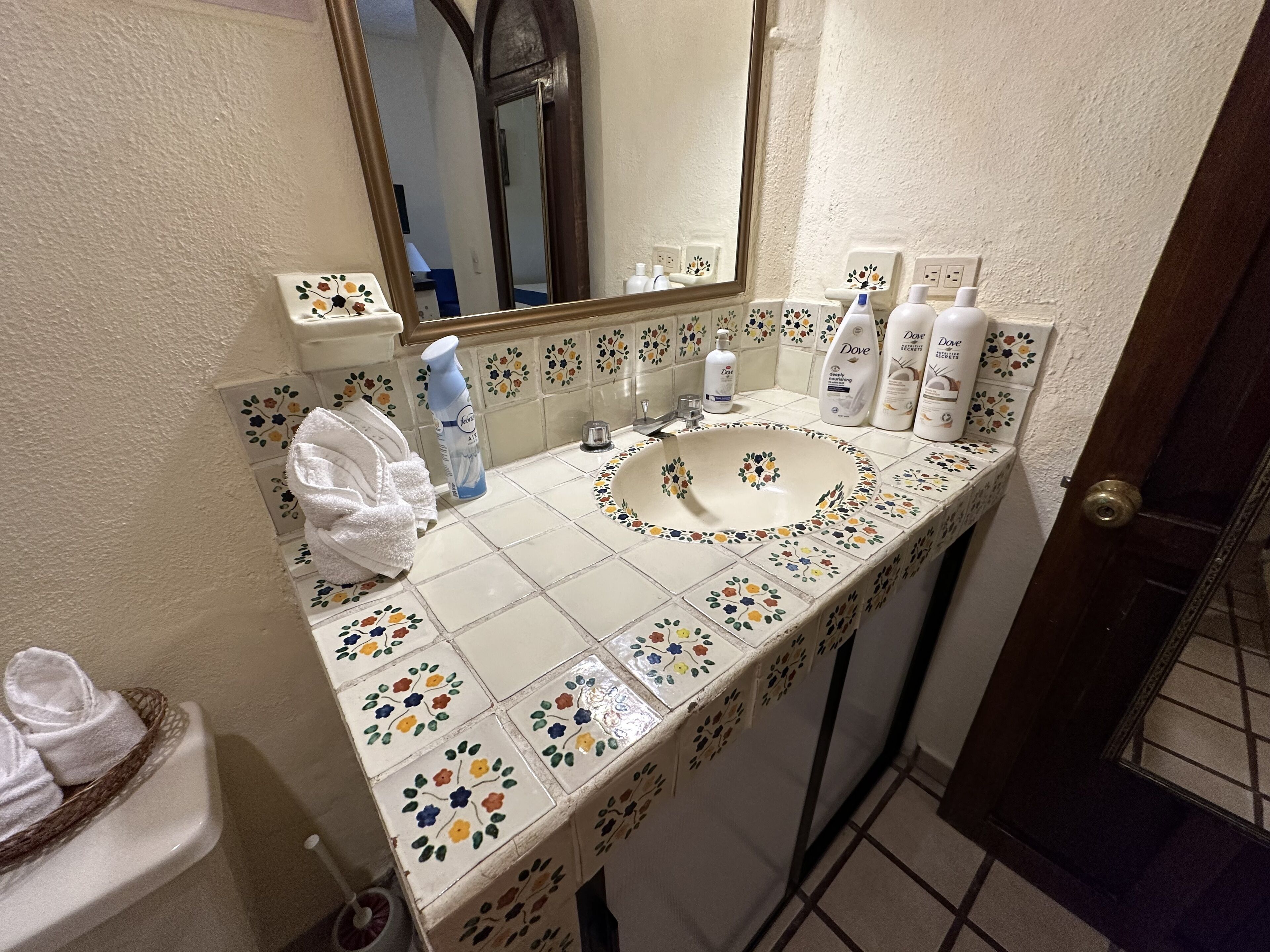 Une salle de bain avec un lavabo blanc, des carreaux à motifs floraux, un miroir et des articles de toilette posés sur le comptoir.
