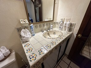 A bathroom with a white sink, floral tiles, a mirror, and toiletries on the counter.