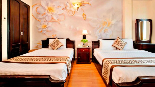 Habitación de hotel con dos camas, una mesita de noche con lámpara, un espejo y una pared decorada con motivos florales.