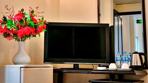 Habitación de hotel con una televisión de pantalla plana, un jarrón de flores rojas, un reloj en la pared y un espejo que refleja la habitación.