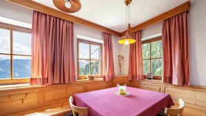 A room with a wooden bench, a table with a pink tablecloth, and large windows with curtains. - Apartment "Innerkaserbach" with Mountain View & Shared Garden (St. Pankraz)