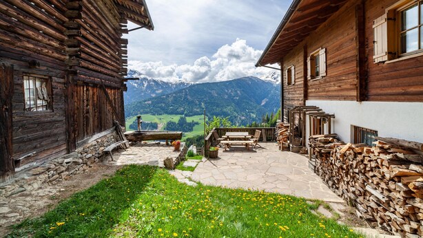 A wooden cabin with a stone patio, a wooden table, and chairs. - Apartment "Innerkaserbach" with Mountain View & Shared Garden (St. Pankraz)