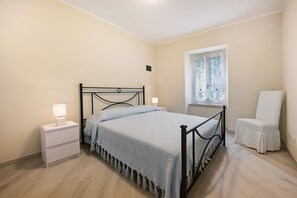 Een slaapkamer met een bed, nachtkastjes, een stoel, een raam en een nachtkastje.