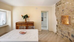 Un comedor con una mesa, sillas, un florero con flores, un aparador de madera y una pared de piedra con un ventanal.