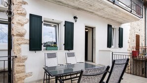 Un comedor con mesa y sillas de vidrio, pared de piedra y contraventanas verdes.