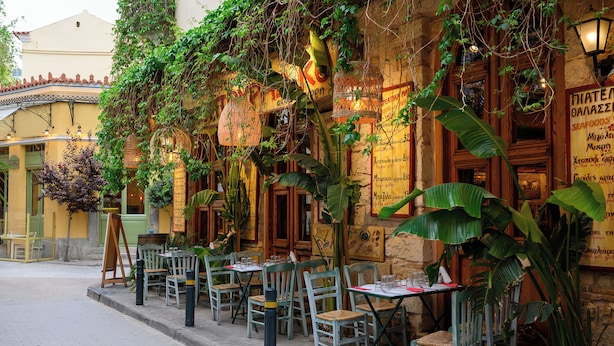 Café al aire libre con mesas y sillas, rodeado de vegetación y detalles arquitectónicos.