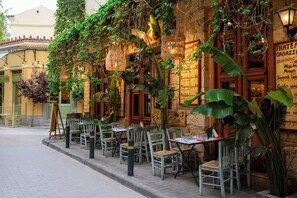 An outdoor cafe with tables and chairs, surrounded by greenery and architectural details. - Psiri Vibes Studios (Athens)