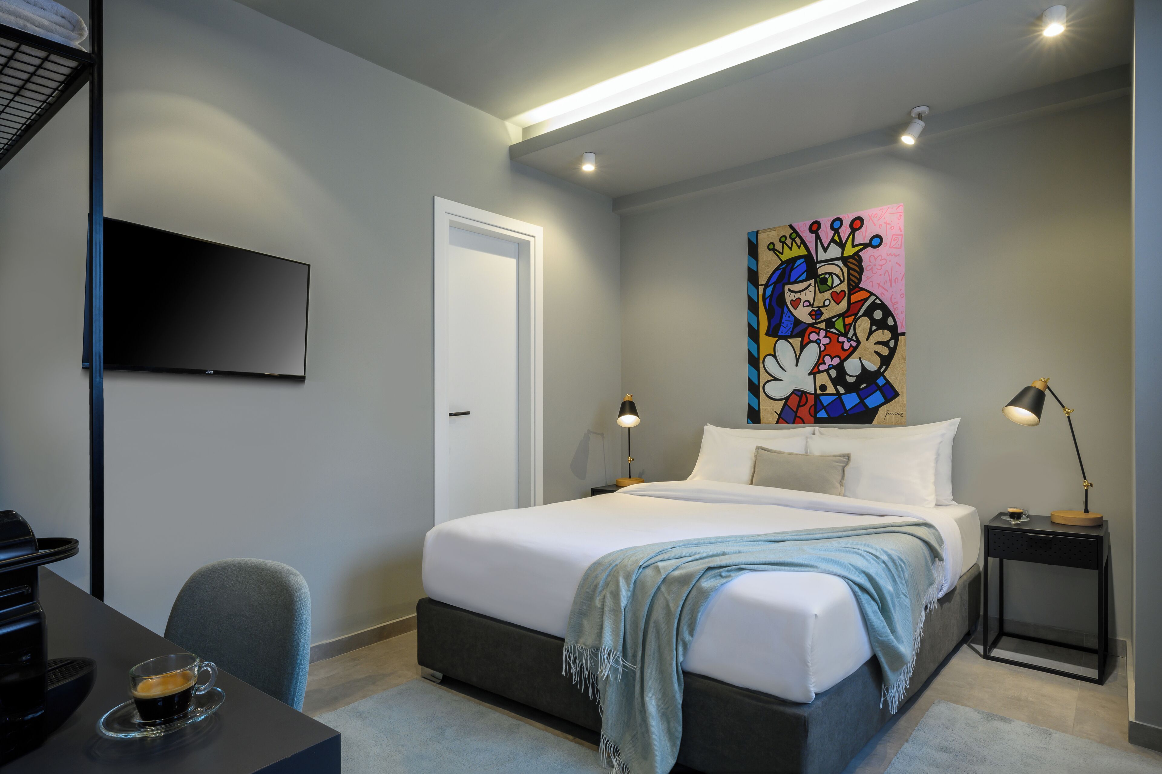A modern bedroom with a bed, bedside tables, a desk, and a flat-screen TV.
