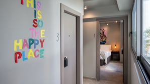 Un pasillo con un letrero colorido que dice "THIS IS SO THE HAPPY PLACE" y una puerta marcada con el número 3.