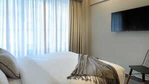 Una habitación de hotel con cama, televisión montada en la pared y una ventana con cortinas.