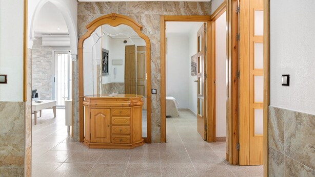 Un pasillo con un tocador de madera, un espejo y una puerta que da a otra habitación.