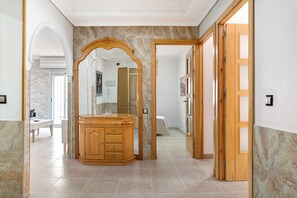 Un couloir avec une coiffeuse en bois, un miroir et une porte donnant sur une autre pièce.
