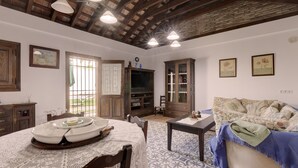 A room with a wooden ceiling, a dining table with a white tablecloth, a patterned floor, and a sofa with a floral throw.