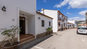 A narrow street lined with white buildings, a parked car, and a potted plant.