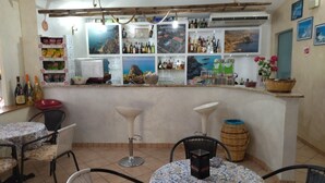 Una zona de bar con suelo de baldosas, taburetes de bar, una mesa redonda con mantel estampado y una variedad de botellas y vasos en estanterías.