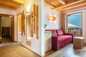 A room with wooden beams, a red plaid sofa, a small table, and a window with a view of a mountain.