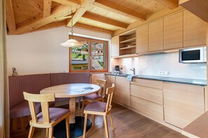 A wooden interior with a dining table, chairs, and a kitchen area including a microwave.
