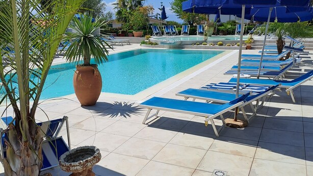 A pool area with lounge chairs and umbrellas, surrounded by palm trees and potted plants. - Apartment 'Agriturismo Heaven Trilocale 1' with Mountain View, Shared Pool and Wi-Fi (ricadi)
