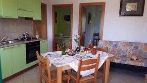 Une cuisine avec des meubles de rangement verts, une table à manger dressée avec des assiettes, des verres et un vase de fleurs.