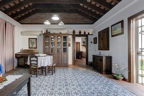 Un comedor con mesa, sillas y suelo estampado. Se observa un mueble de madera con puertas de cristal y un techo con vigas a la vista.