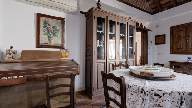 A dining area with a wooden table, chairs, a cabinet with glass doors, and a framed picture on the wall.