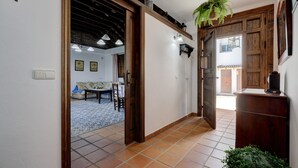 A hallway with a tiled floor, wooden doors, a hanging plant, and a sofa in the background.