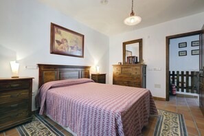 Un dormitorio con cama, cómoda, mesita de noche, lámpara y un cuadro en la pared.