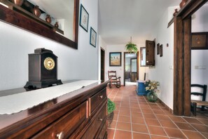 Un pasillo con un aparador de madera, un reloj, cuadros enmarcados, una silla y una planta en maceta.