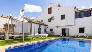A swimming pool with lounge chairs, a patio area, and a white building with multiple windows and a tiled roof.