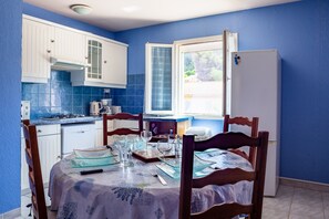 Una cocina con paredes azules, armarios blancos, una mesa de comedor con vasos y platos, y un refrigerador.