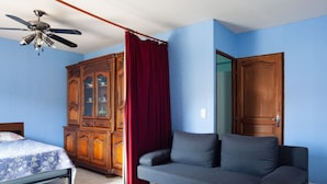 A room with a bed, a sofa, a wooden cabinet, a ceiling fan, and a door.