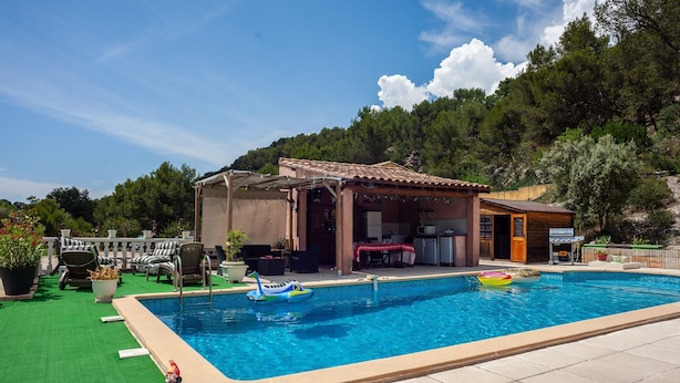 A swimming pool with a lounge area, outdoor seating, and a view of a forested hillside.