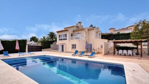 A swimming pool with lounge chairs and umbrellas, a two-story building with balconies, and a pergola with chairs. - Villa 'Casa Leuki' with Sea/Mountain Views, Pool, Garden, Wi-Fi & AC (Calpe)