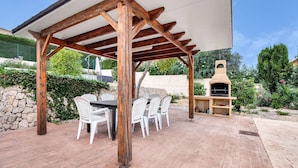 A covered outdoor patio with a wooden pergola, a barbecue grill, and a dining table with chairs. - Villa 'Casa Leuki' with Sea/Mountain Views, Pool, Garden, Wi-Fi & AC (Calpe)