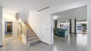 Un intérieur moderne avec un escalier, un espace de vie doté d’un canapé et une vue sur l’extérieur, visible à travers une porte.