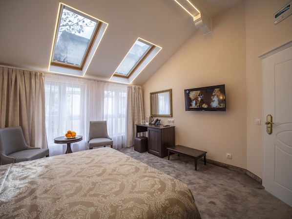 A hotel room with a large bed, two chairs, a small table with fruit, a desk with a mirror, a TV, and a door. - The Moon Boutique Hotel (Sofia)