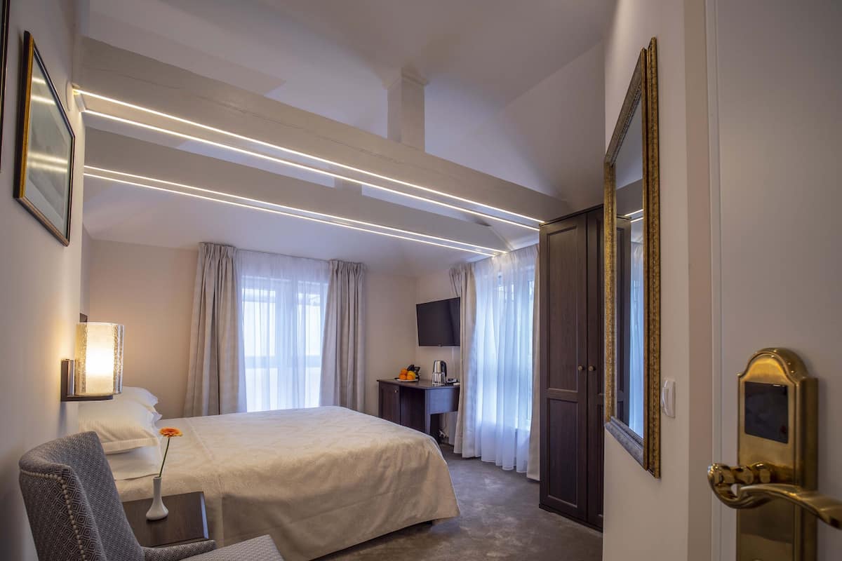 A hotel room with a large bed, a desk with a chair, a television, and a wardrobe.