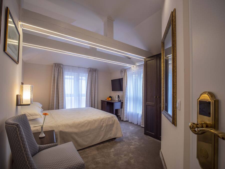A hotel room with a large bed, a desk with a chair, a television, and a wardrobe.