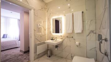 A modern bathroom with a marble wall, a sink, a toilet, and a shower.