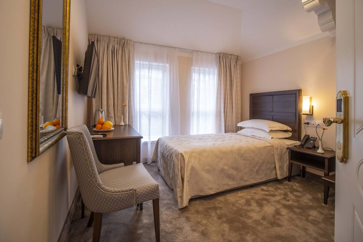 A hotel room with a bed, a chair, a desk with a lamp, and a telephone.