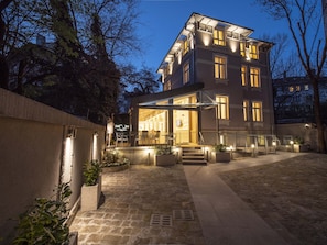 A multi-story hotel with a well-lit entrance, outdoor seating area, and a stone-paved courtyard. - The Moon Boutique Hotel (Sofia)