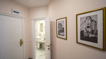 Een hal met een witte deur, een badkamer met een wastafel en spiegel, en twee zwart-wit foto's in lijsten aan de muur.