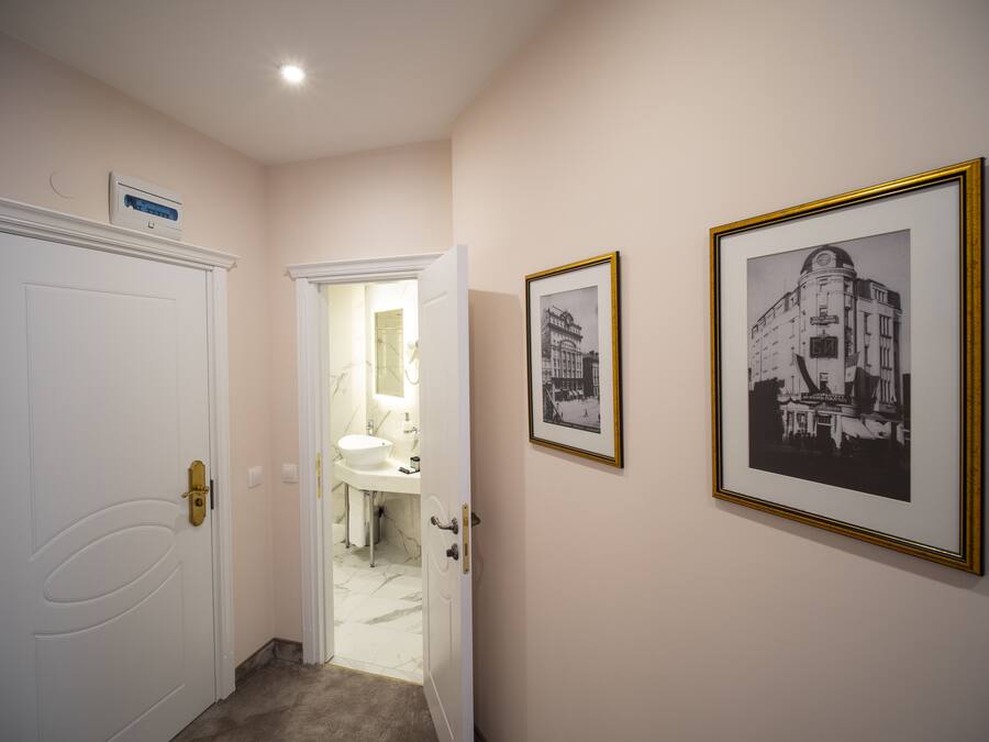 Een hal met een witte deur, een badkamer met een wastafel en spiegel, en twee zwart-wit foto's in lijsten aan de muur.