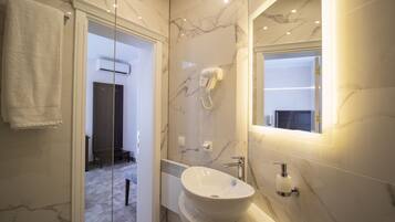 A modern bathroom with a glass shower enclosure, a white sink with a marble countertop, and a hairdryer mounted on the wall.