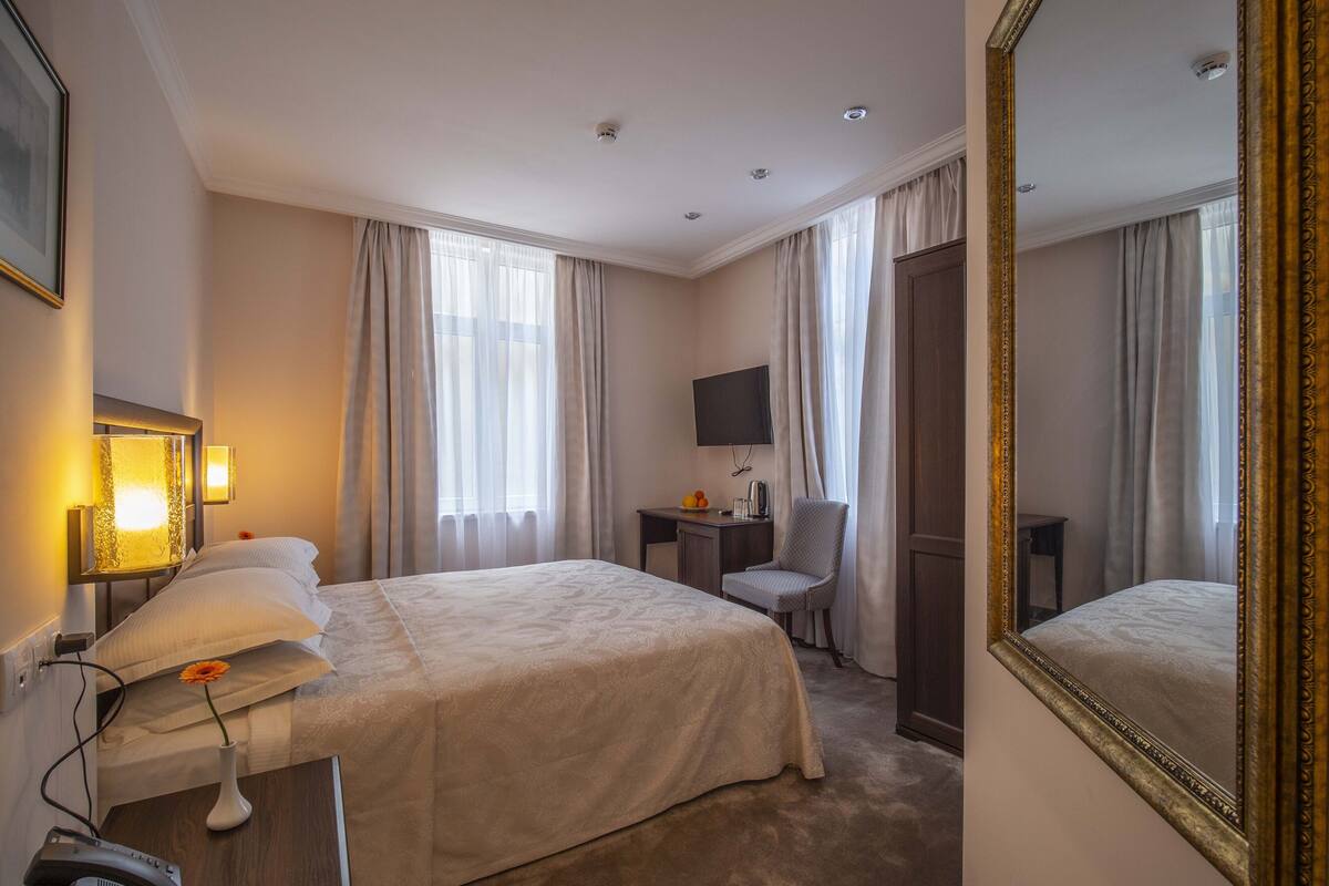A hotel room with a large bed, a desk with a chair, a TV, and a mirror.