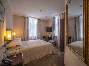 Een hotelkamer met een groot bed, een bureau met stoel, een televisie en een spiegel.