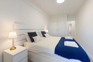 A neatly made bed with pillows, a bedside lamp, and a blue throw blanket.