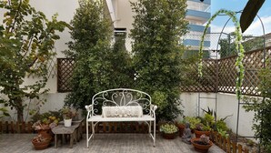 Eine Terrasse mit einer weißen Metallbank, Blumentöpfen und einem Holzzaun.